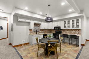 Kitchen featuring glass insert cabinets, white cabinetry, decorative backsplash, black appliances, and stone tile floors