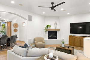 Living room with light wood-style floors, arched walkways, a fireplace, a ceiling fan, and a chandelier
