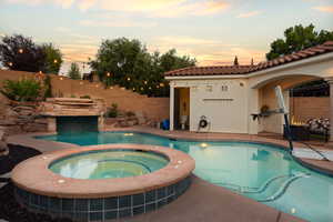 Pool at dusk featuring a fenced backyard, a patio area, and a pool with connected hot tub