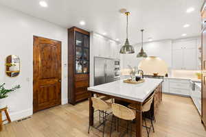Dual tone kitchen with two tone cabinetry, a kitchen island with sink, glass insert cabinets, decorative backsplash, and light stone counters