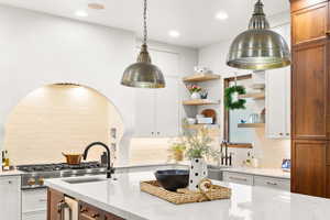 Dual tone kitchen with light stone counters, open shelves, dual tone cabinets, hanging light fixtures, and tasteful backsplash
