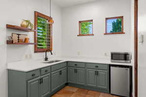 Kitchen featuring refrigerator, stainless steel microwave, decorative light fixtures, green cabinetry, and tile patterned floors