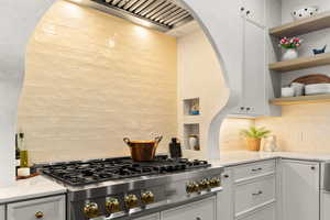 Kitchen featuring white cabinetry, stainless steel gas cooktop, open shelves, light stone countertops, and tasteful backsplash