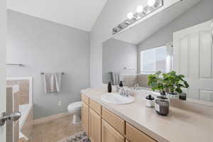 Bathroom with a bath, lofted ceiling, vanity, and light tile patterned floors