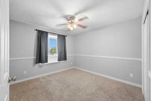 Carpeted spare room featuring ceiling fan and baseboards