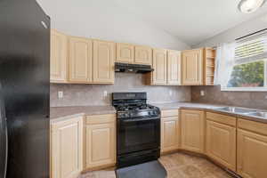 Kitchen with black appliances, lofted ceiling, light wood finish cabinetry, and tasteful backsplash