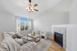 Living area with light wood-style flooring, lofted ceiling, ceiling fan, and a tiled fireplace