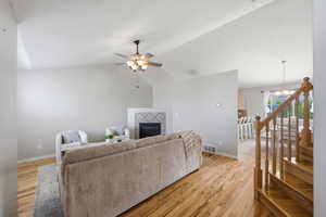 Living area with light wood-type flooring, vaulted ceiling, a fireplace, a ceiling fan, and suspended lighting
