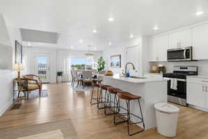Kitchen featuring stainless steel appliances, white cabinetry, light wood finished floors, and a center island with sink
