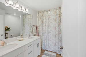 Full bath with double vanity, light wood-style flooring, and curtained shower