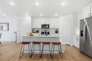 Kitchen with stainless steel appliances, light wood-style flooring, white cabinetry, a center island with sink, and a kitchen breakfast bar