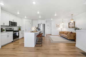 Kitchen featuring stainless steel appliances, white cabinetry, a kitchen island with sink, light wood-type flooring, and open floor plan