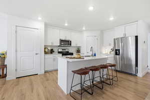 Kitchen with stainless steel appliances, white cabinetry, light wood-type flooring, a kitchen breakfast bar, and an island with sink