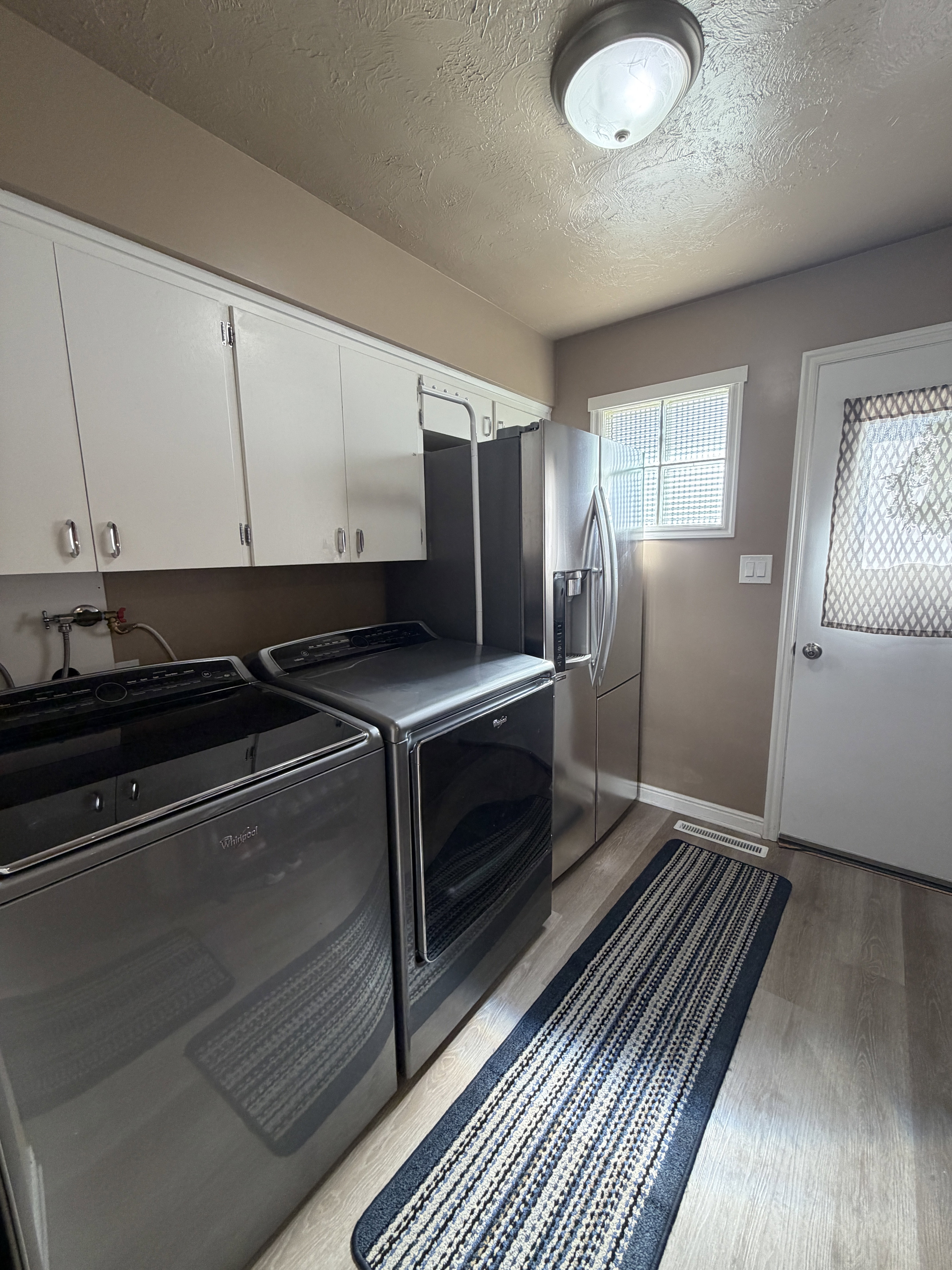 Laundry area featuring a textured ceiling, light wood-style flooring, separate washer and dryer, and cabinet space, entry from the west and door to the east patio