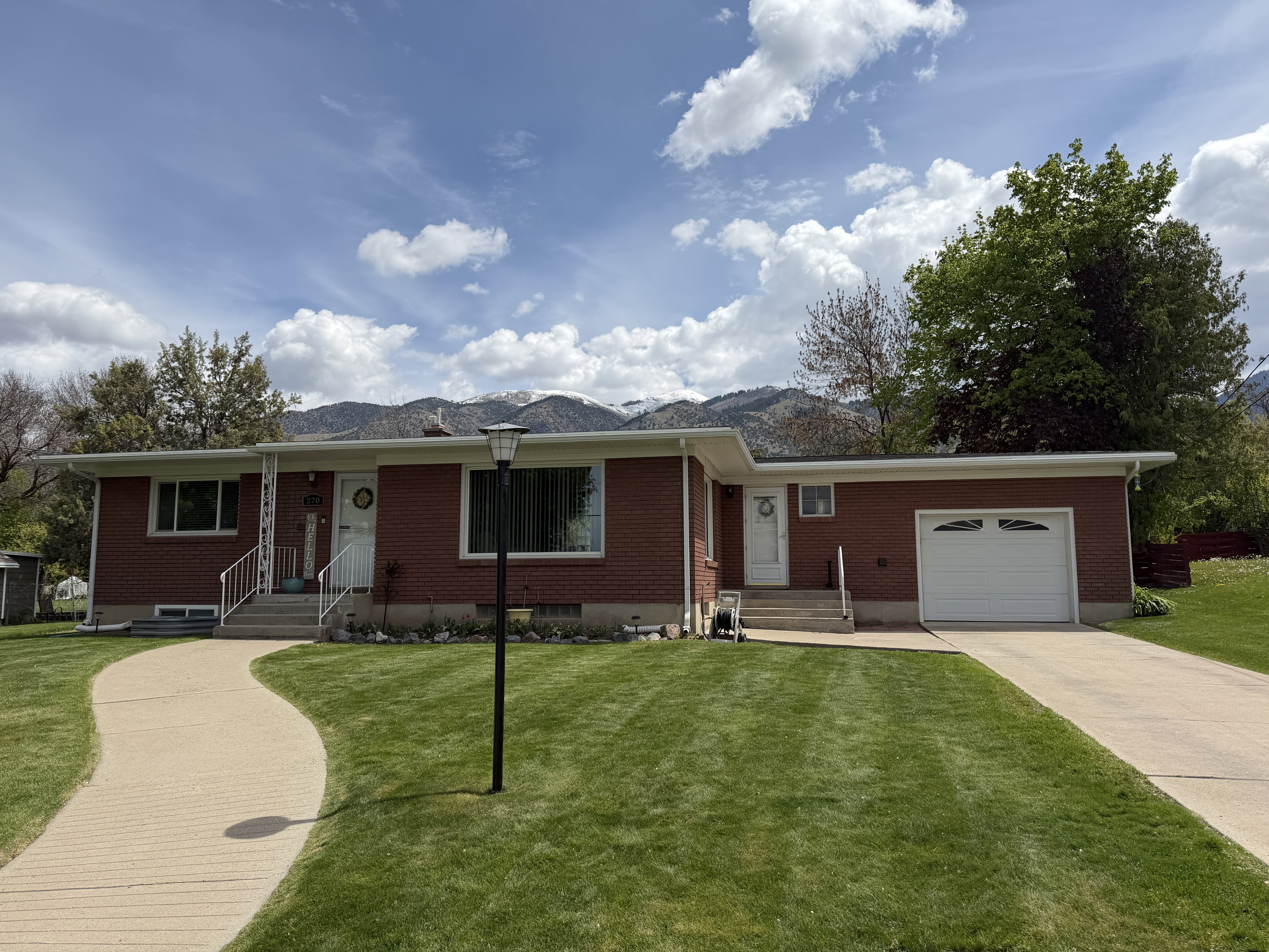 Ranch-style house with brick siding, an attached garage, a front yard, concrete driveway, and a mountain view