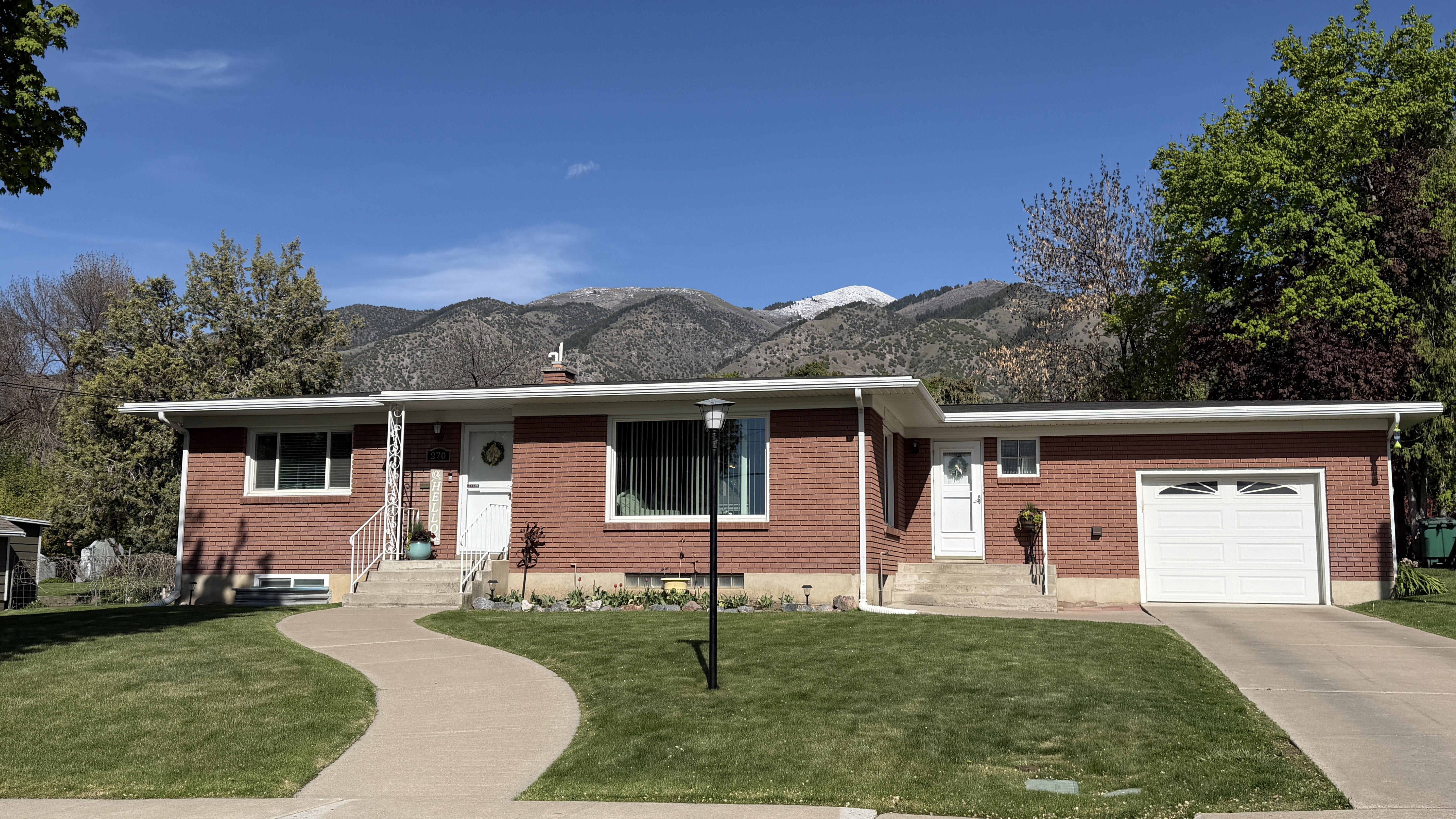 Single story home featuring an attached garage, a front yard, concrete driveway, brick siding, and a mountain view