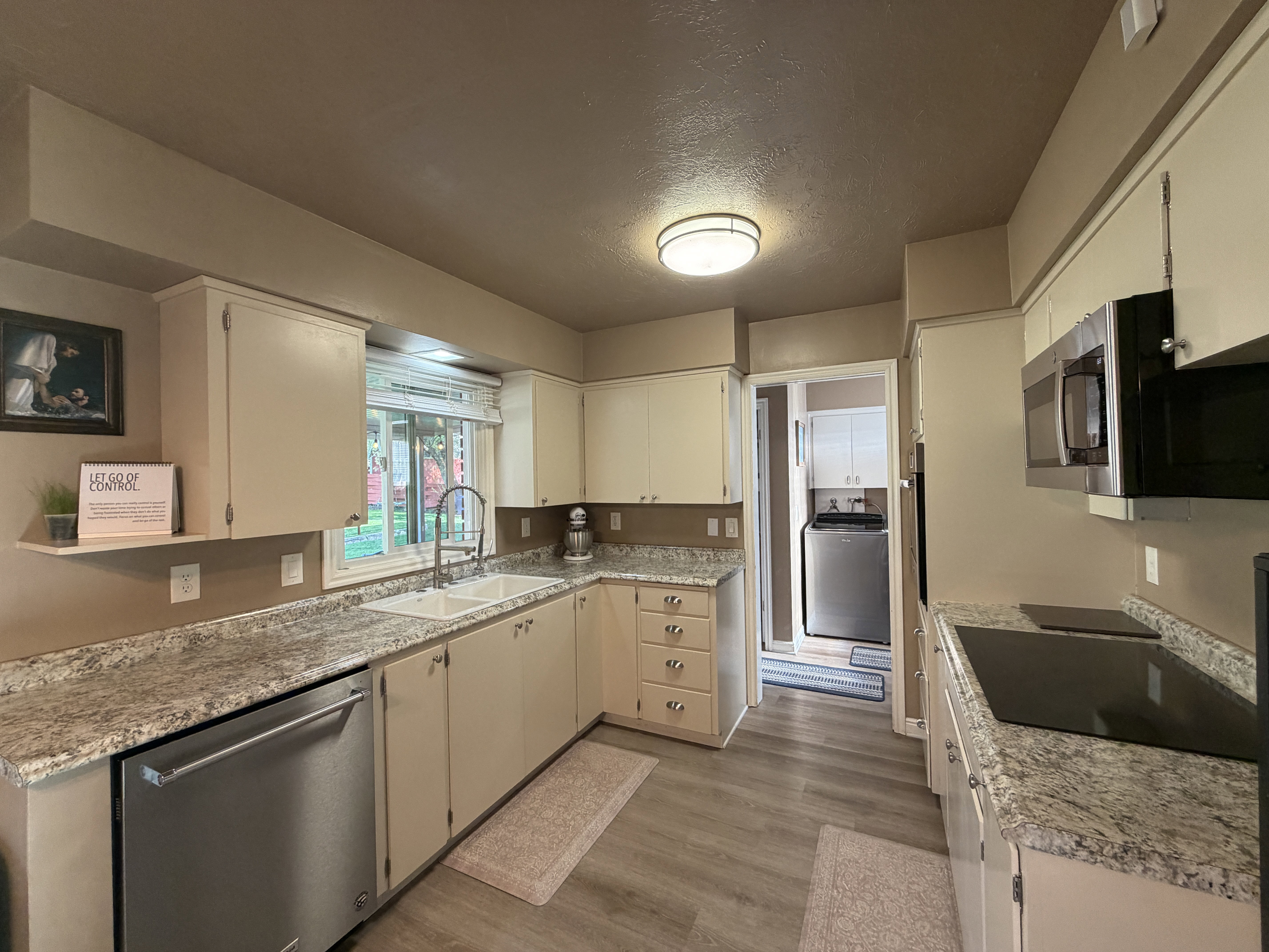 Kitchen featuring dishwasher, black electric cooktop, light wood-style floors, washer / clothes dryer, and a textured ceiling