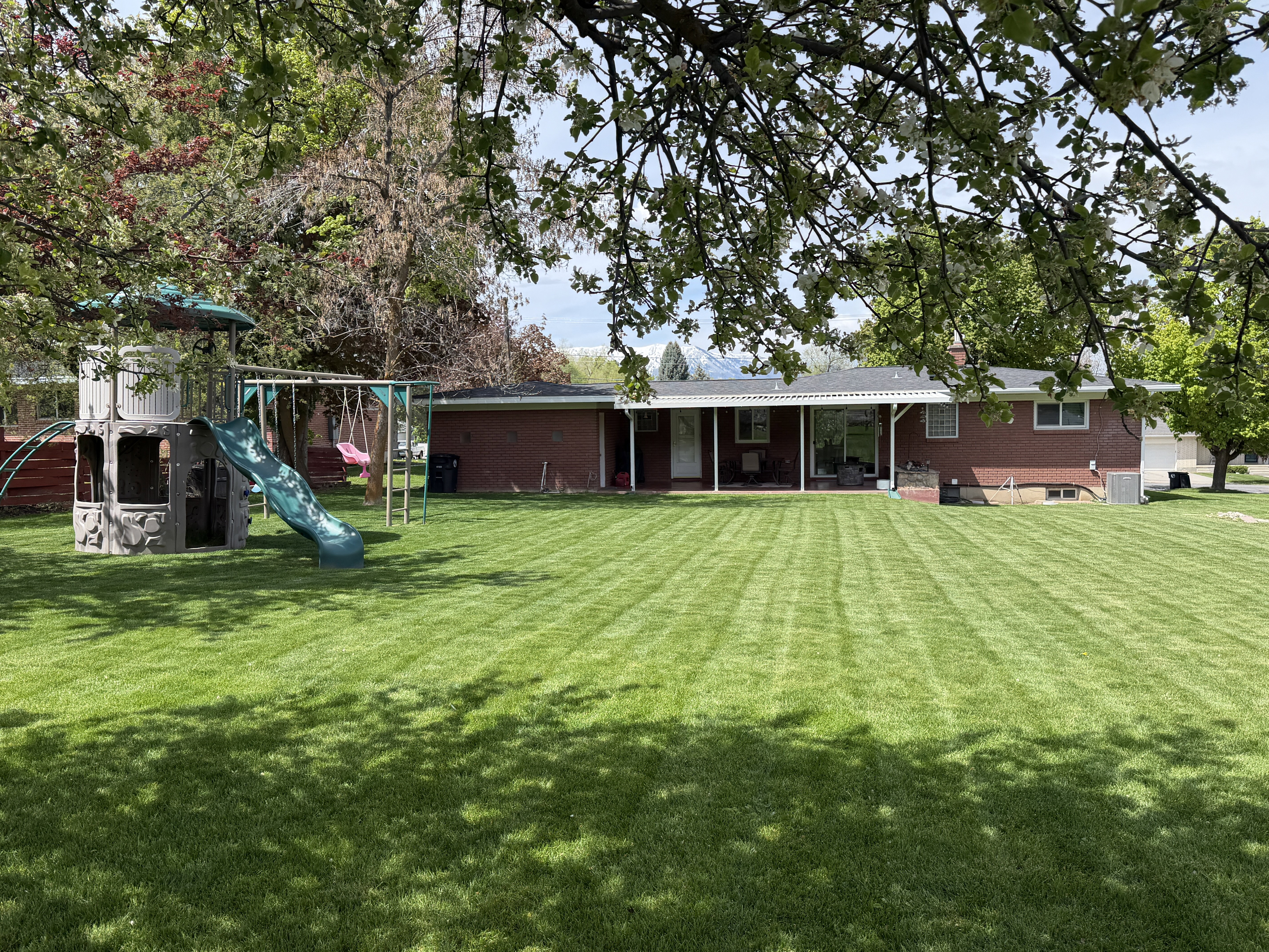 Rear view of property with a lawn, a playground, brick siding, and a chimney