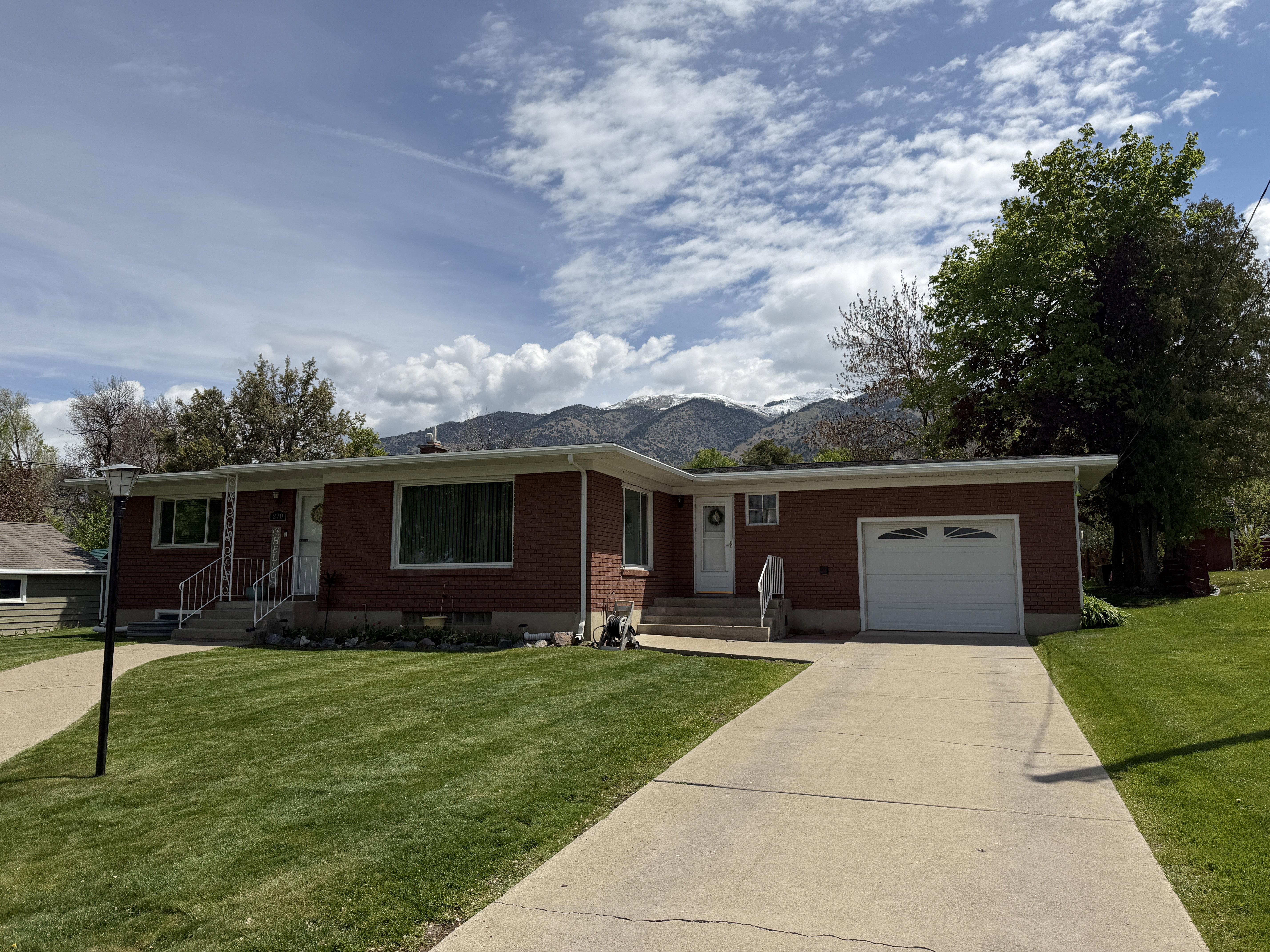 Single story home featuring brick siding, an attached garage, a front yard, concrete driveway, and a mountain view