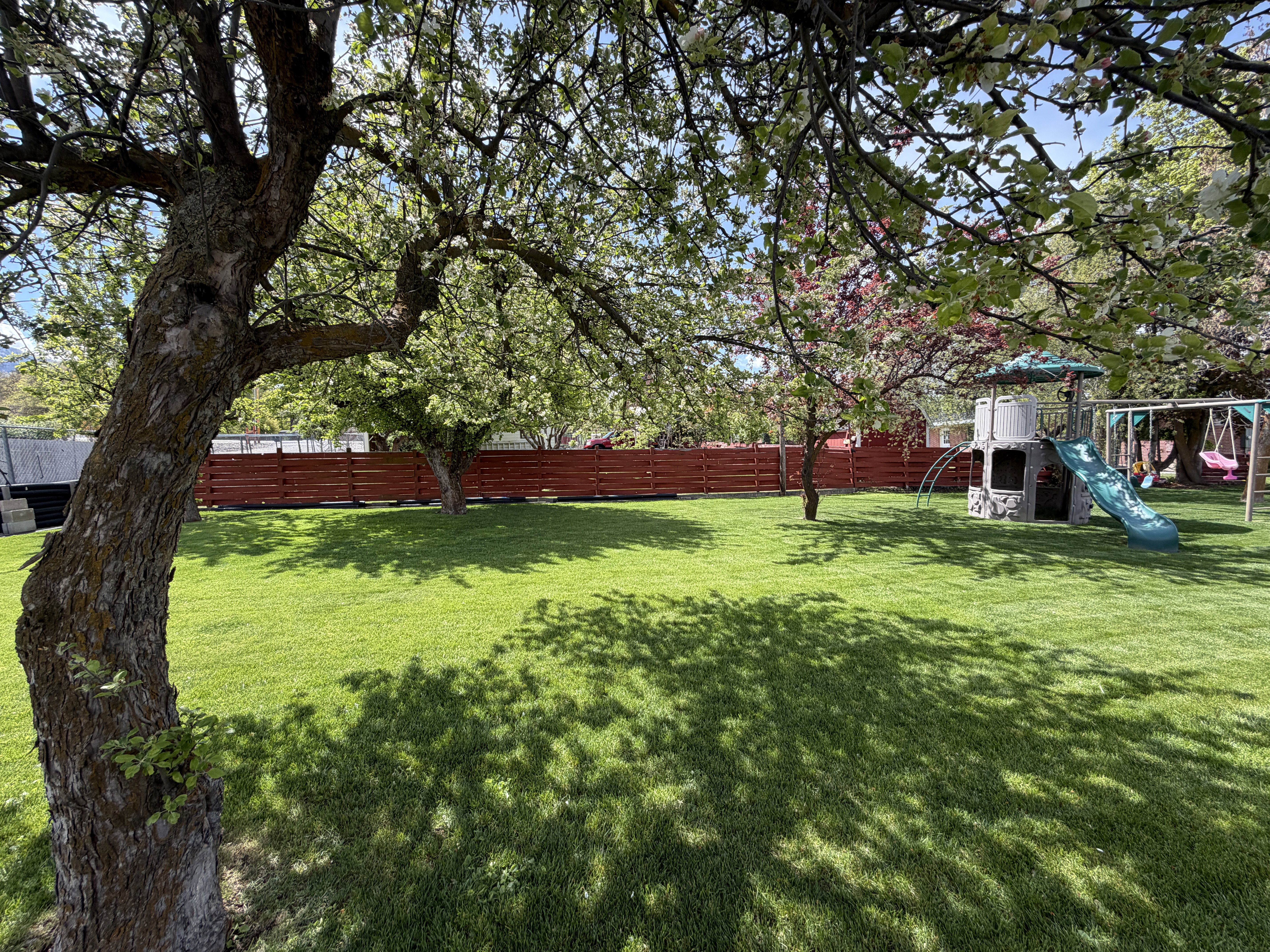 Partially fenced backyard with a playground and mature trees