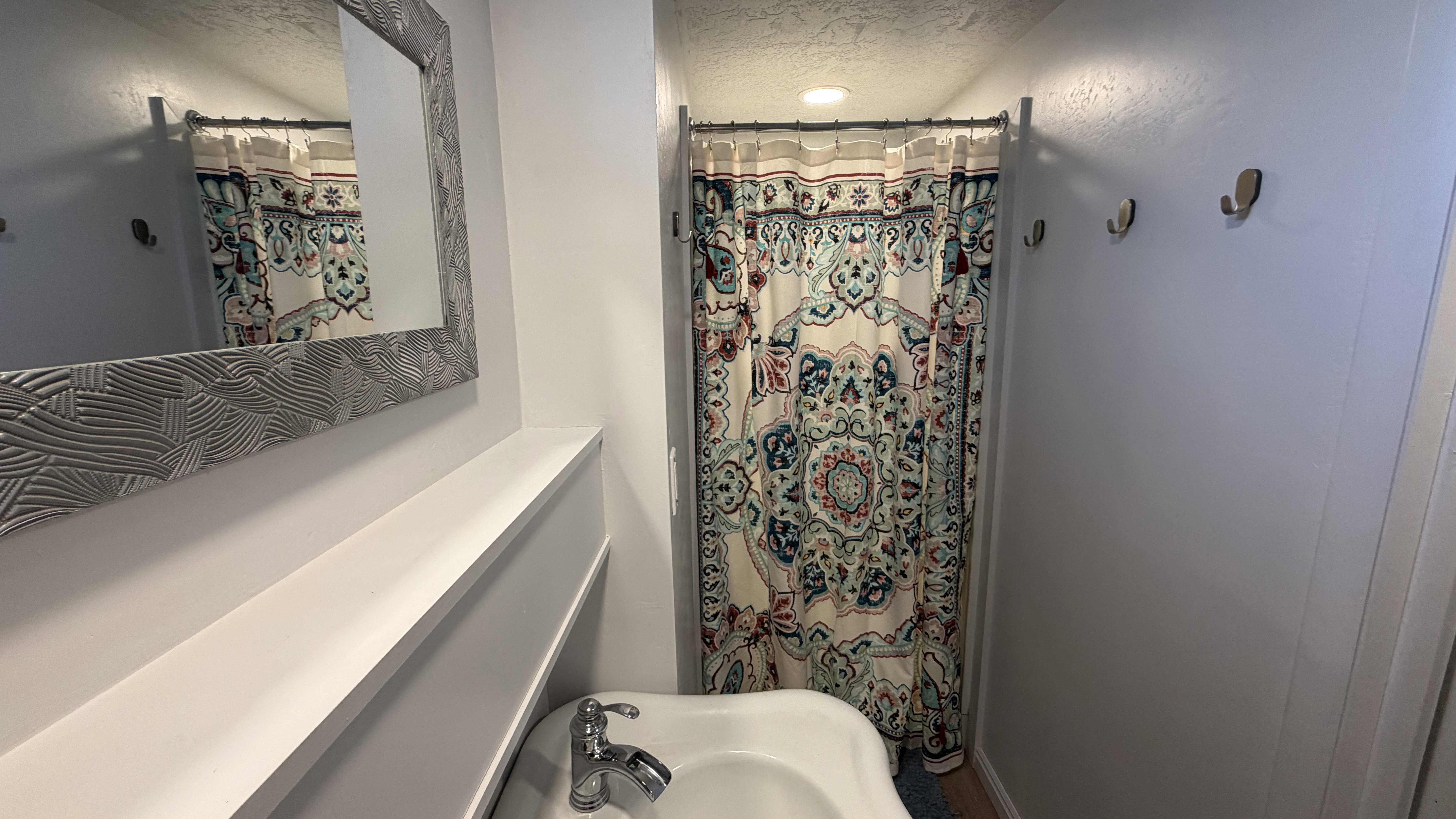 3/4 bath with curtained shower and a textured ceiling, large pedestal sink