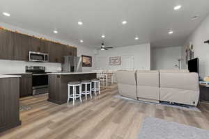 Kitchen featuring a center island, open floor plan, a kitchen bar, stainless steel appliances, and light wood-style floors