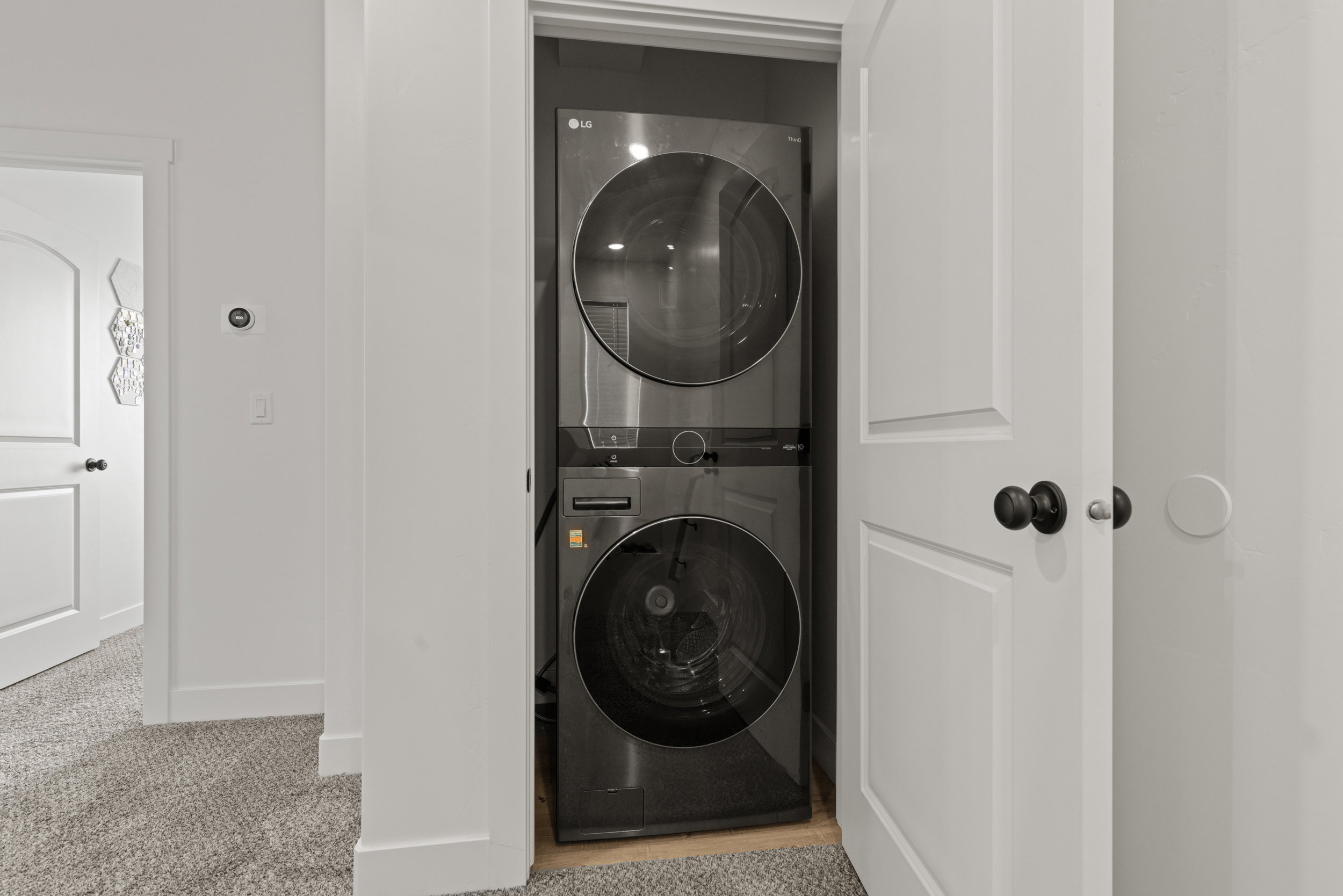 Laundry area with stacked washer and clothes dryer and light carpet