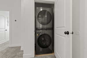Laundry area with stacked washer and clothes dryer and light carpet