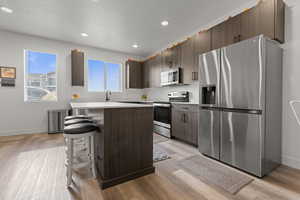 Kitchen featuring stainless steel appliances, dark wood finish cabinets, a center island, a breakfast bar, and light wood-style flooring