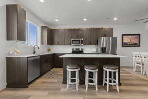 Kitchen with a kitchen breakfast bar, stainless steel appliances, light wood-style floors, a center island, and recessed lighting