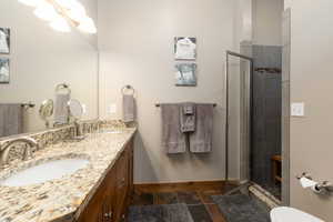 Full bath featuring double vanity, a shower stall, and stone tile floors