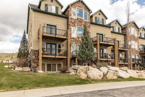Rear view of property featuring stone siding, a balcony, a yard, and french doors