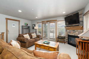 Carpeted living room featuring a stone fireplace and recessed lighting