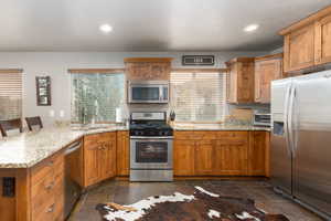 Kitchen featuring a peninsula, stainless steel appliances, light stone counters, a breakfast bar, and wood finish cabinets