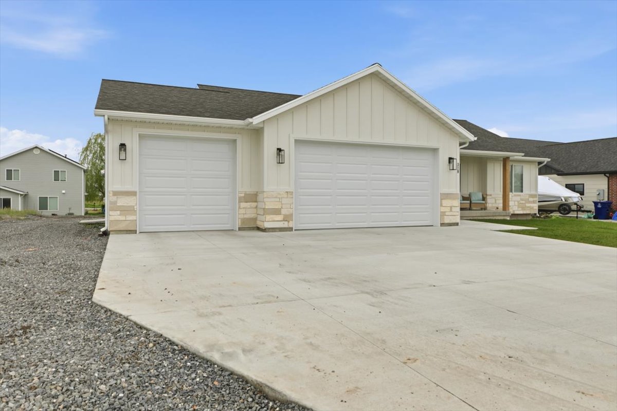 Ranch-style home featuring board and batten siding, a garage, stone siding, and driveway