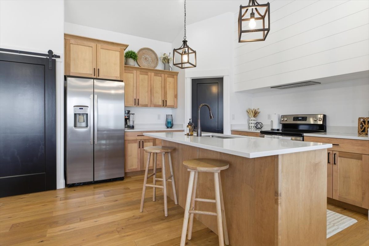 Kitchen featuring stainless steel appliances, an island with sink, light wood-type flooring, decorative light fixtures, and a kitchen breakfast bar