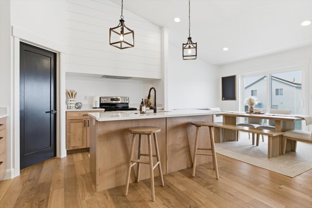 Kitchen featuring a kitchen island with sink, hanging light fixtures, light wood-style flooring, lofted ceiling, and a kitchen bar