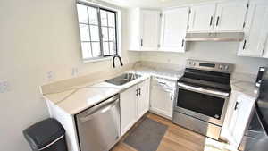 Kitchen featuring stainless steel appliances, light stone counters, white cabinets, and light wood-type flooring