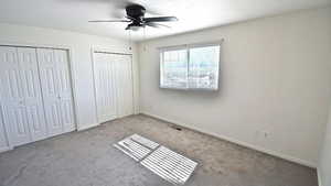 Unfurnished bedroom with two closets, carpet, and a ceiling fan