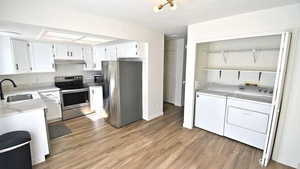 Kitchen with stainless steel appliances, white cabinets, light wood-type flooring, washing machine and dryer, and open shelves