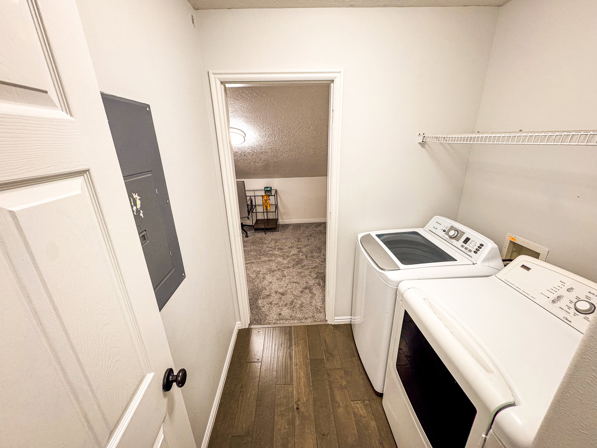 Laundry area featuring a textured ceiling, dark wood finished floors, washing machine and clothes dryer, and electric panel