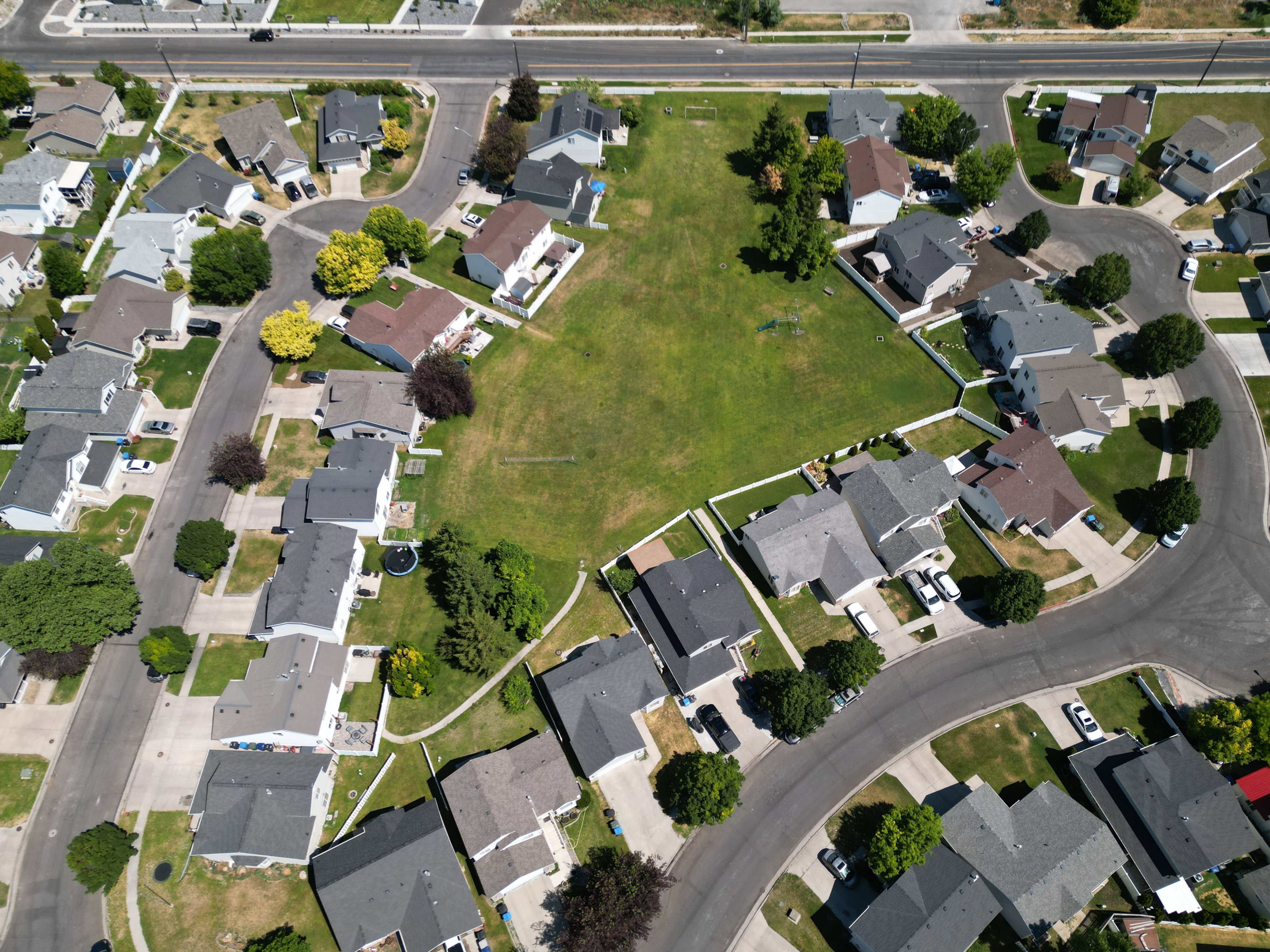 Expansive green lot surrounded by residential properties, featuring paved streets and mature trees