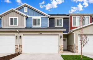 Multi-story townhome exterior featuring an attached two-car garage, stone veneer accents, and vinyl siding