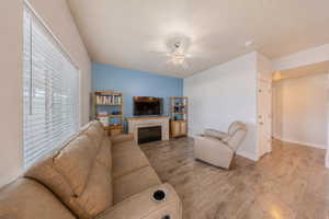 Living area featuring wood-finish flooring, a wall-mounted television above a fireplace, and a ceiling fan