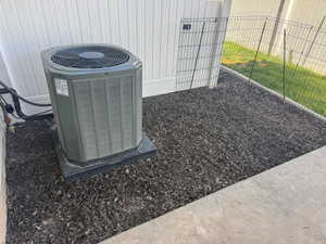 Central air conditioning unit on a concrete pad, surrounded by dark wood mulch and a white privacy fence