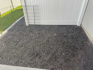 Landscaped area featuring dark mulch, a white vinyl fence, and a wire perimeter fence