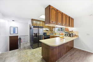 Kitchen with wood finish cabinetry, a peninsula, stainless steel fridge, light countertops, and black electric range oven