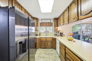 Kitchen with stainless steel fridge, light countertops, wood finish cabinetry, white dishwasher, and black range