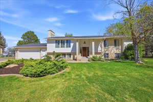 Split Level featuring covered porch, brick siding, a chimney, and a front lawn