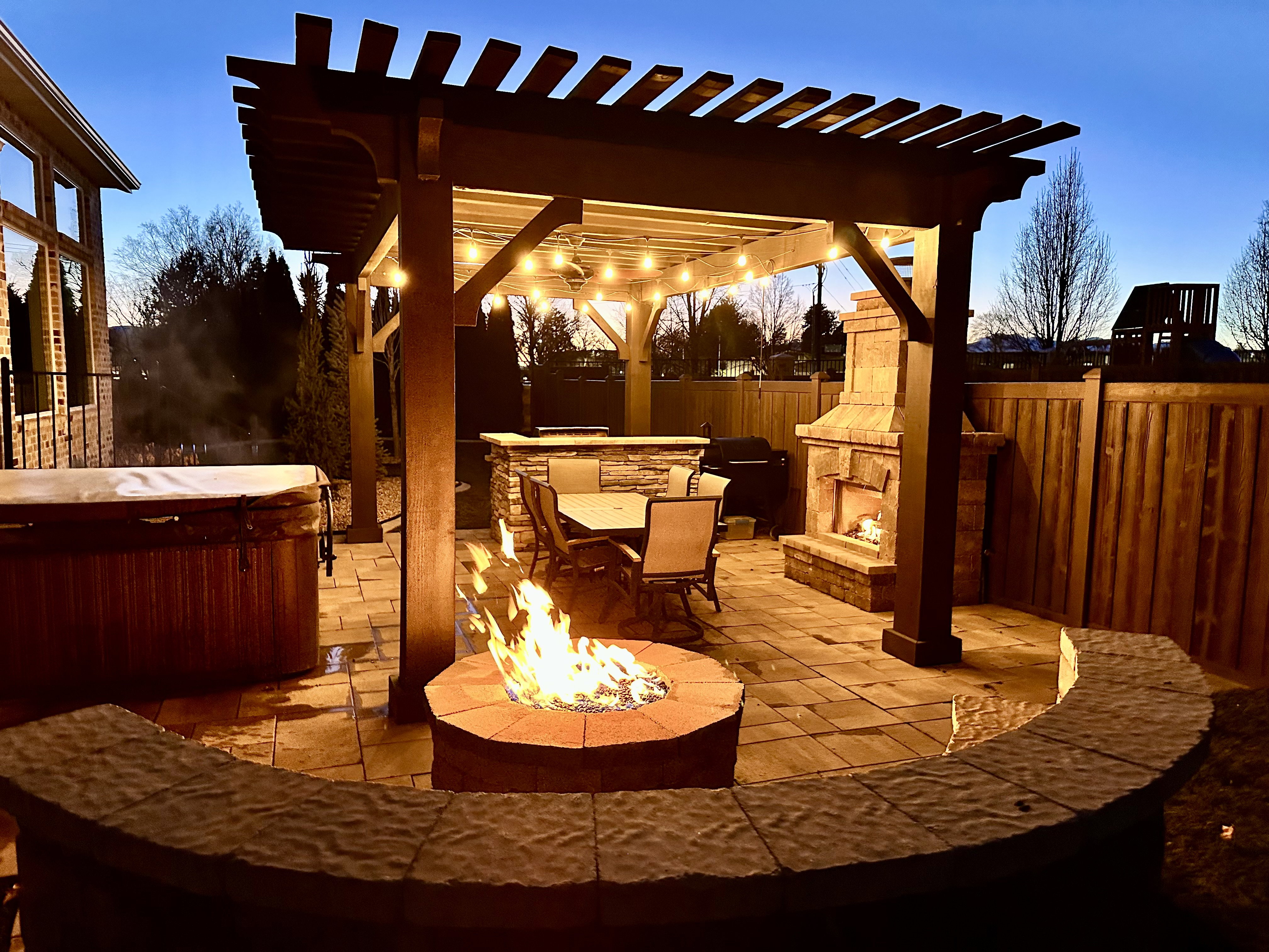 Patio terrace at dusk featuring a patio area, a hot tub, BBQ, a fire pit, and a pergola